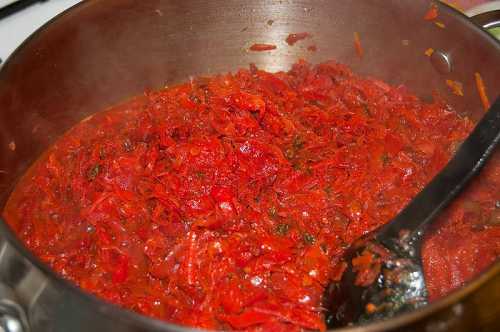 Затем плотно уложите помидоры, залейте кипятком и дайте остыть. Добавьте в банки порезанный на дольки чеснок, соль, сахар, уксусную кислоту, снова залейте кипятком и закатайте